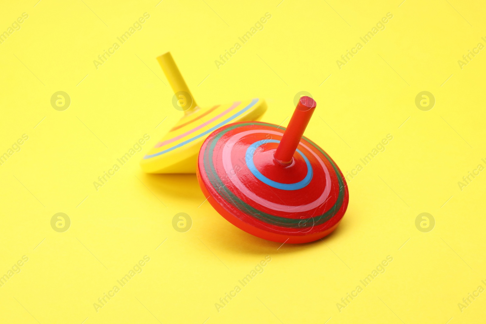 Photo of Two bright spinning tops on yellow background. Toy whirligig