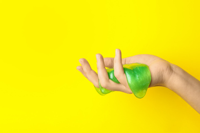 Photo of Woman playing with green slime on yellow background, closeup. Antistress toy