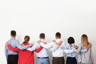 Photo of Group of young people hugging each other on light background. Teamwork concept