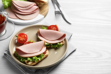 Plate of tasty sandwiches with boiled sausage, tomato and lettuce on white wooden table. Space for text