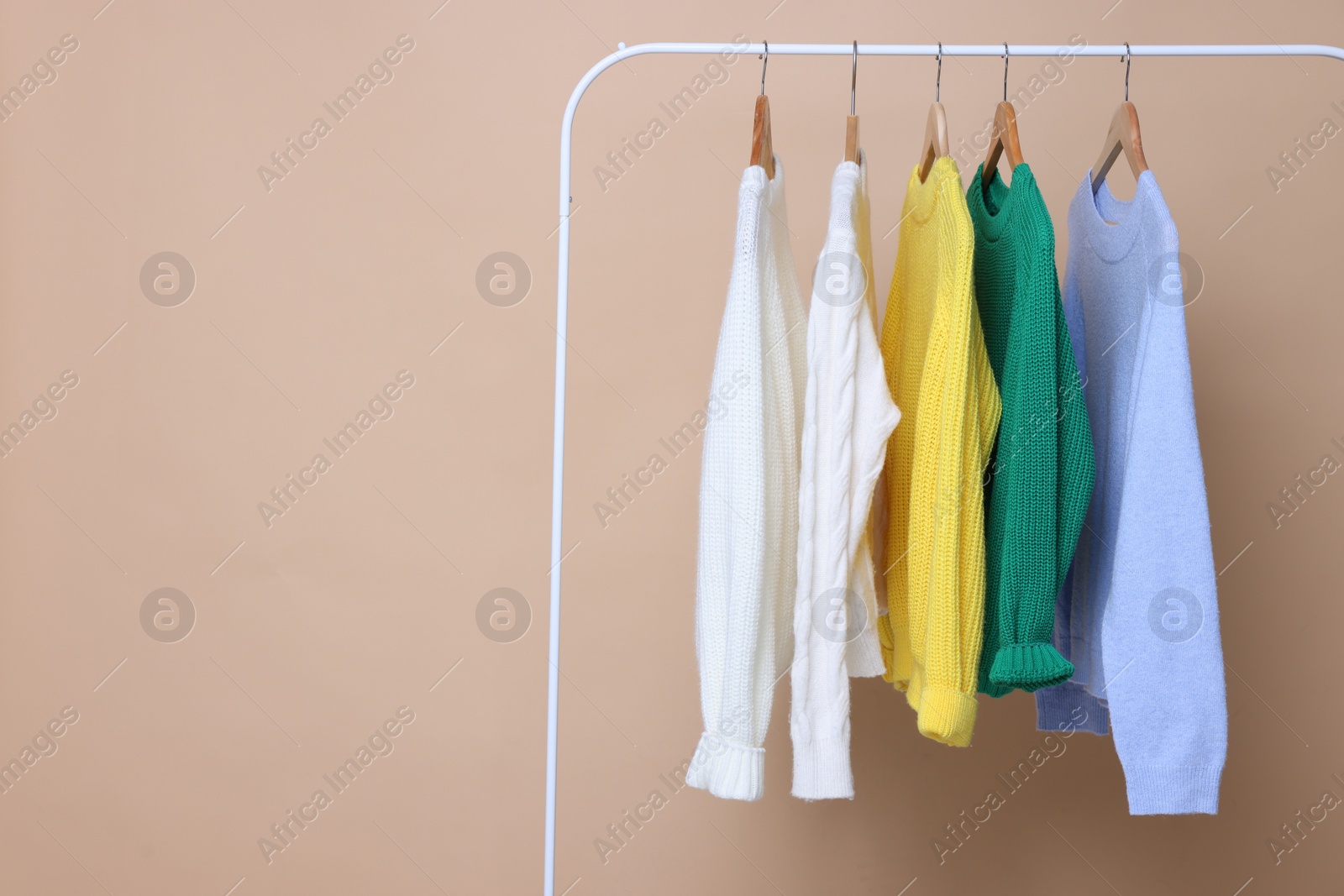 Photo of Rack with different warm sweaters on beige background. Space for text