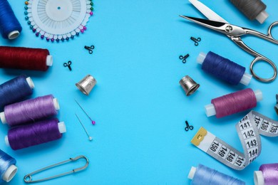 Flat lay composition with thimbles and different sewing tools on light blue background. Space for text