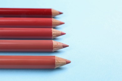 Different lip pencils on light blue background, closeup view with space for text. Cosmetic product