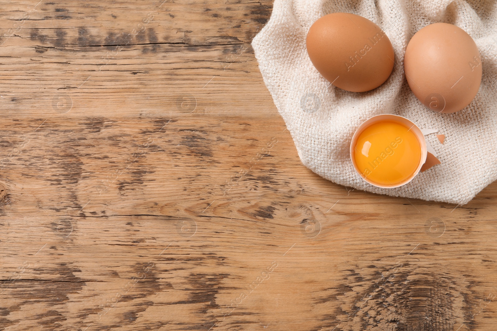 Photo of Whole and cracked eggs on wooden table, flat lay. Space for text