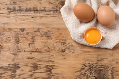 Photo of Whole and cracked eggs on wooden table, flat lay. Space for text