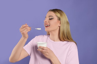 Photo of Woman eating tasty yogurt on violet background
