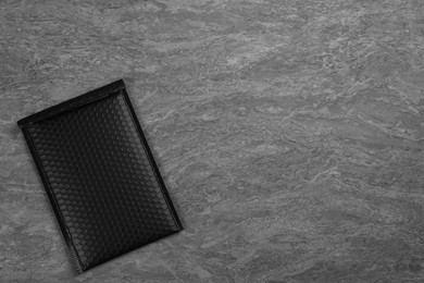 Photo of Black padded envelope with bubble wrap on grey background, top view. Space for text