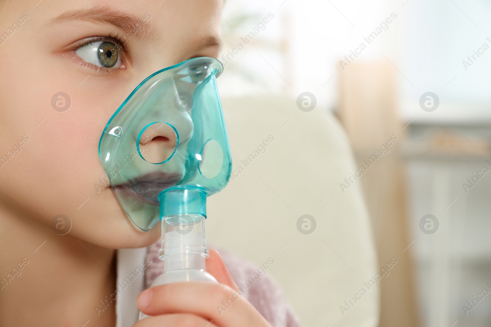 Photo of Little girl using nebulizer for inhalation indoors, closeup