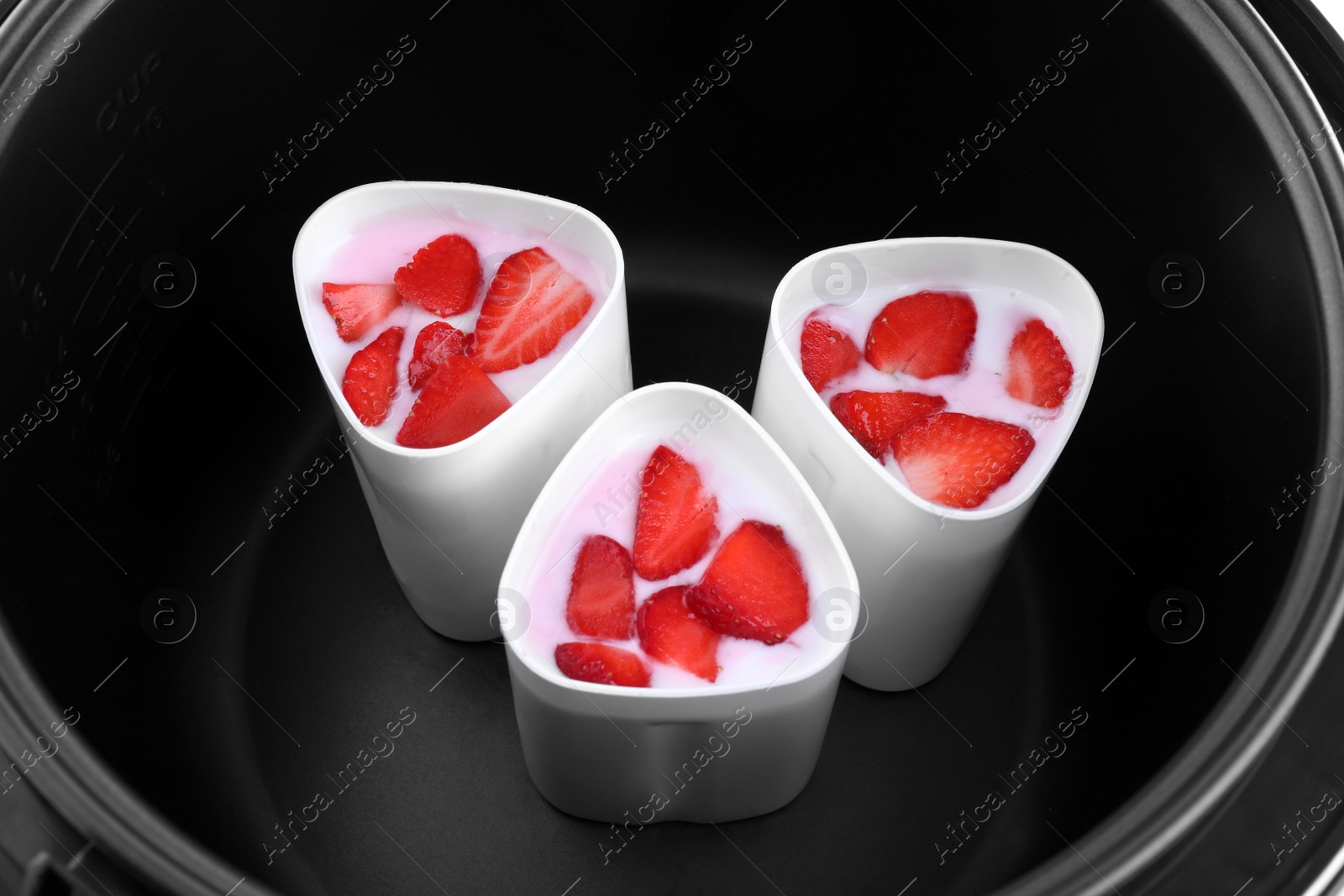 Photo of Cups of homemade strawberry yogurt in modern multi cooker, closeup view