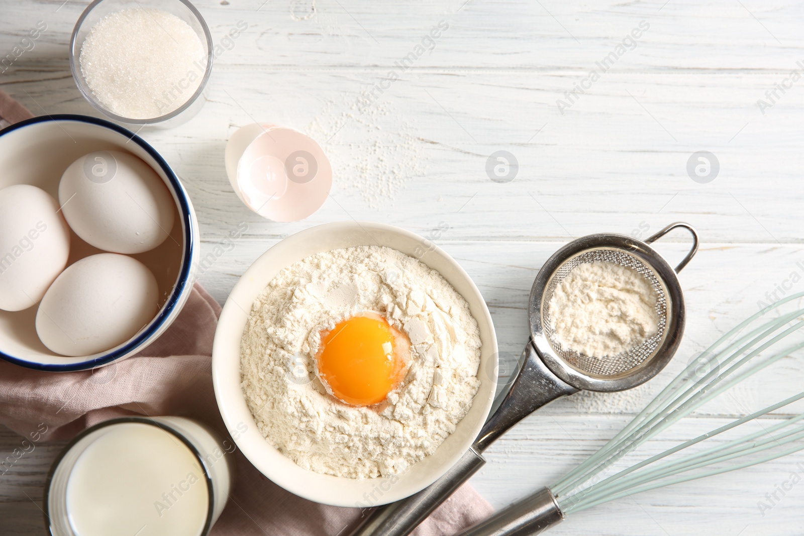 Photo of Flour with yolk in bowl and other ingredients for dough on white wooden table, flat lay