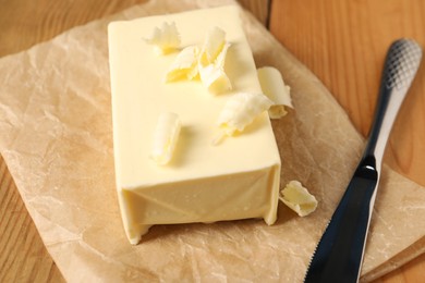 Tasty butter and knife on wooden table, closeup