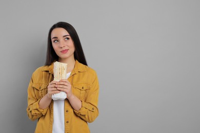 Dreamy young woman holding tasty shawarma on grey background. Space for text