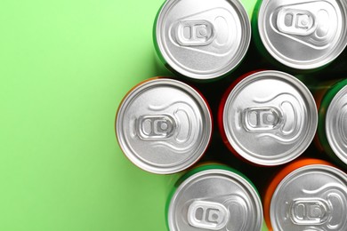 Photo of Energy drink in cans on light green background, top view. Space for text