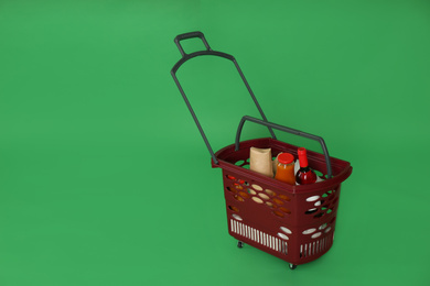 Shopping basket full of different products on green background. Space for text