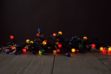 Photo of Beautiful glowing Christmas lights on wooden table against black background