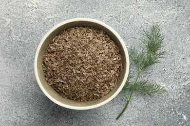 Photo of Bowl of dry seeds and fresh dill on grey table, flat lay