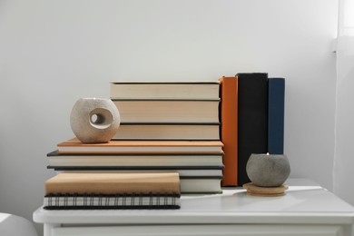 Photo of Hardcover books and scented candles on white bedside table indoors