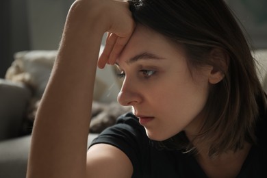 Photo of Sad young woman near sofa at home, closeup