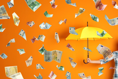 Image of Woman holding umbrella under money rain on color background, closeup 