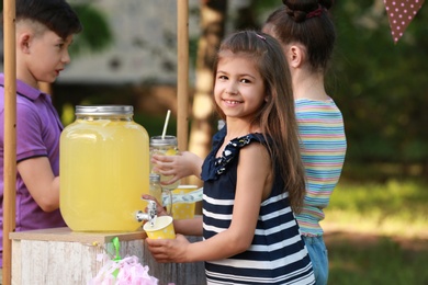 Photo of Cute little girl pouring natural lemonade into cup in park. Summer refreshing drink