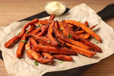 Photo of Board with delicious sweet potato fries and sauce on wooden table, closeup