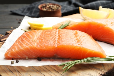 Photo of Wooden board with tasty salmon fillet on dark table, closeup