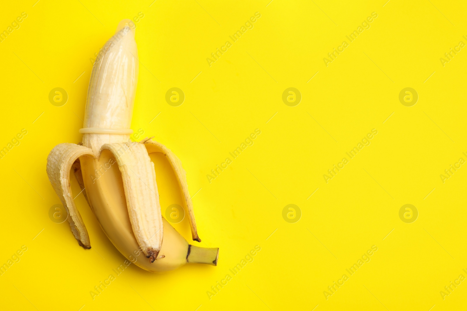 Photo of Banana with condom and space for text on yellow background, top view. Safe sex