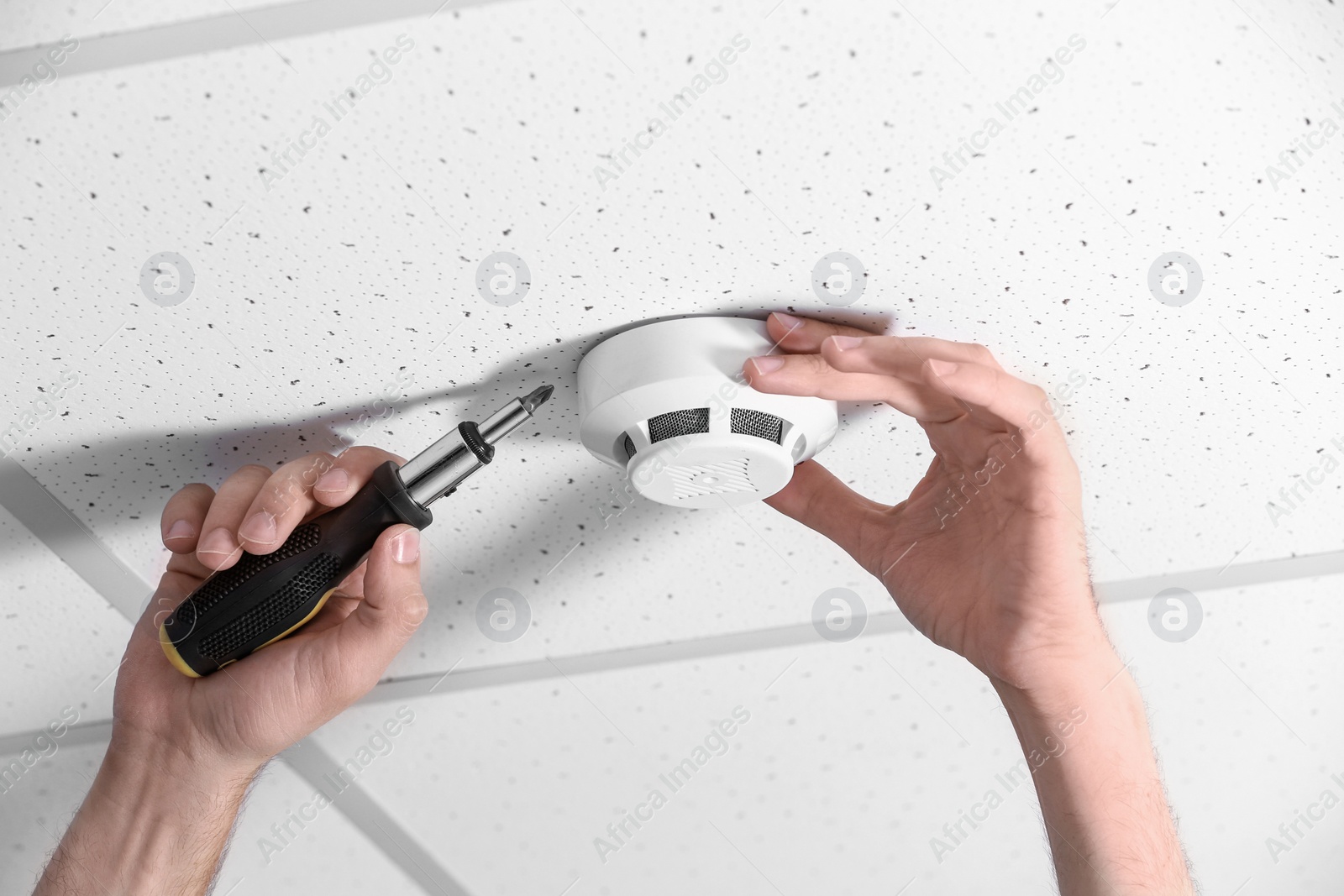 Photo of Young male technician installing smoke alarm system indoors