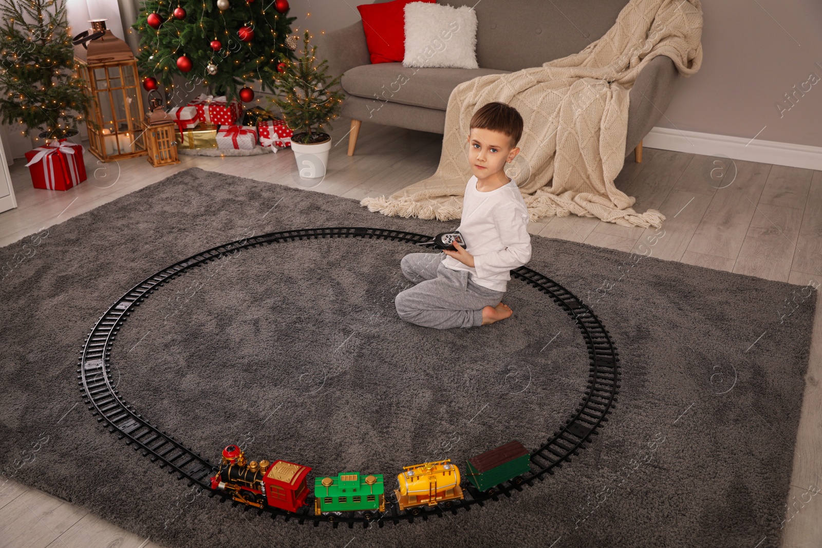 Photo of Little boy playing with colorful train toy in room decorated for Christmas