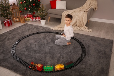 Photo of Little boy playing with colorful train toy in room decorated for Christmas