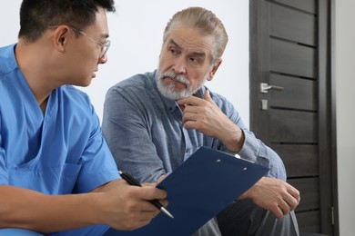 Photo of Doctor with clipboard consulting senior patient in clinic