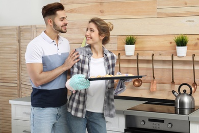 Photo of Young couple with baking sheet of homemade cookies near oven in kitchen