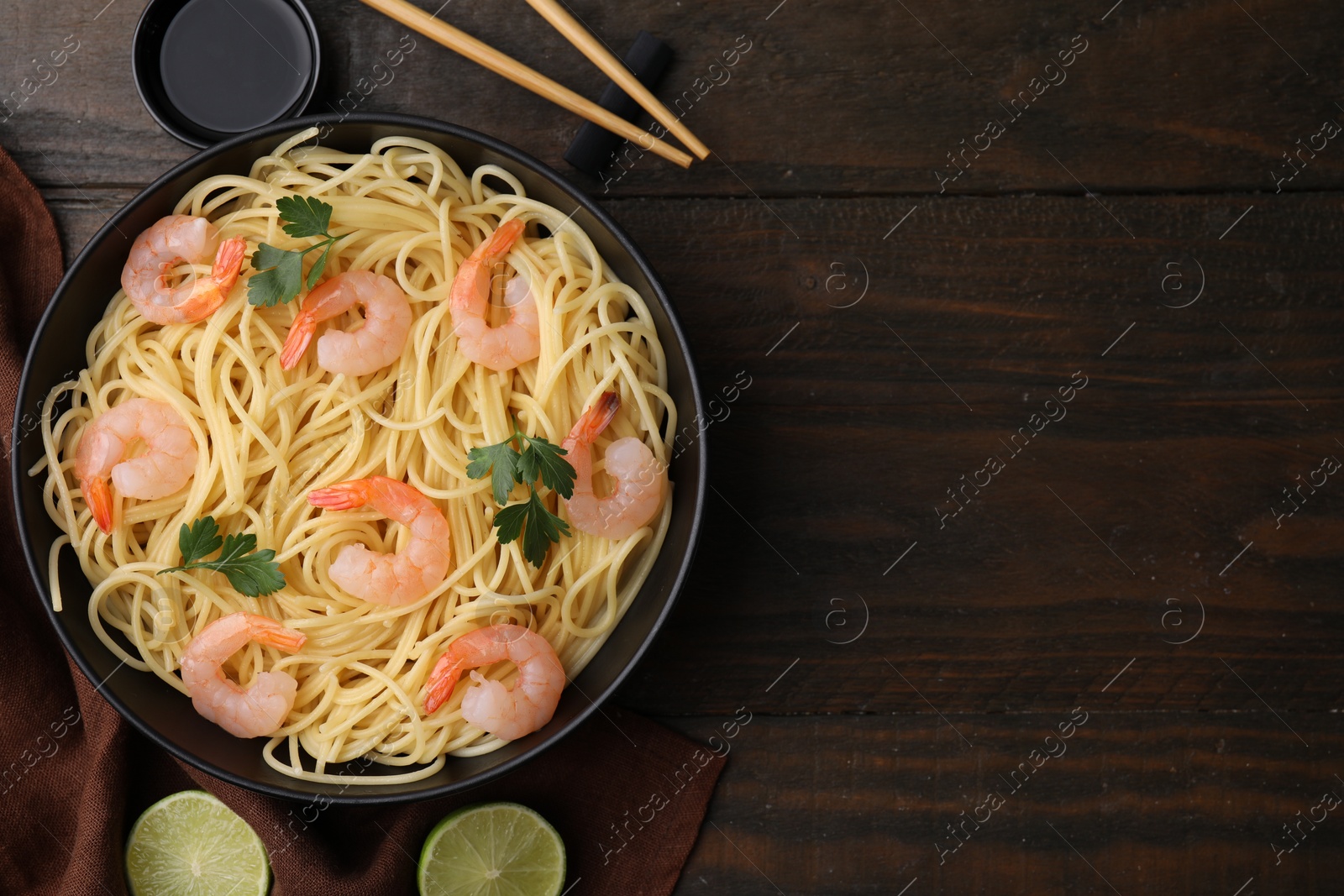 Photo of Tasty spaghetti with shrimps, parsley, lime and soy sauce on wooden table, flat lay. Space for text