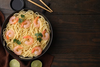 Photo of Tasty spaghetti with shrimps, parsley, lime and soy sauce on wooden table, flat lay. Space for text