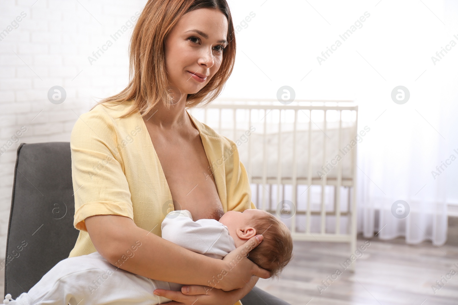 Photo of Young woman breast feeding her little baby at home. Space for text