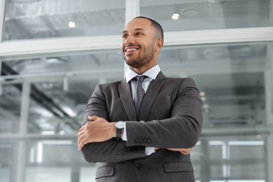 Happy man with crossed arms in office, low angle view. Lawyer, businessman, accountant or manager