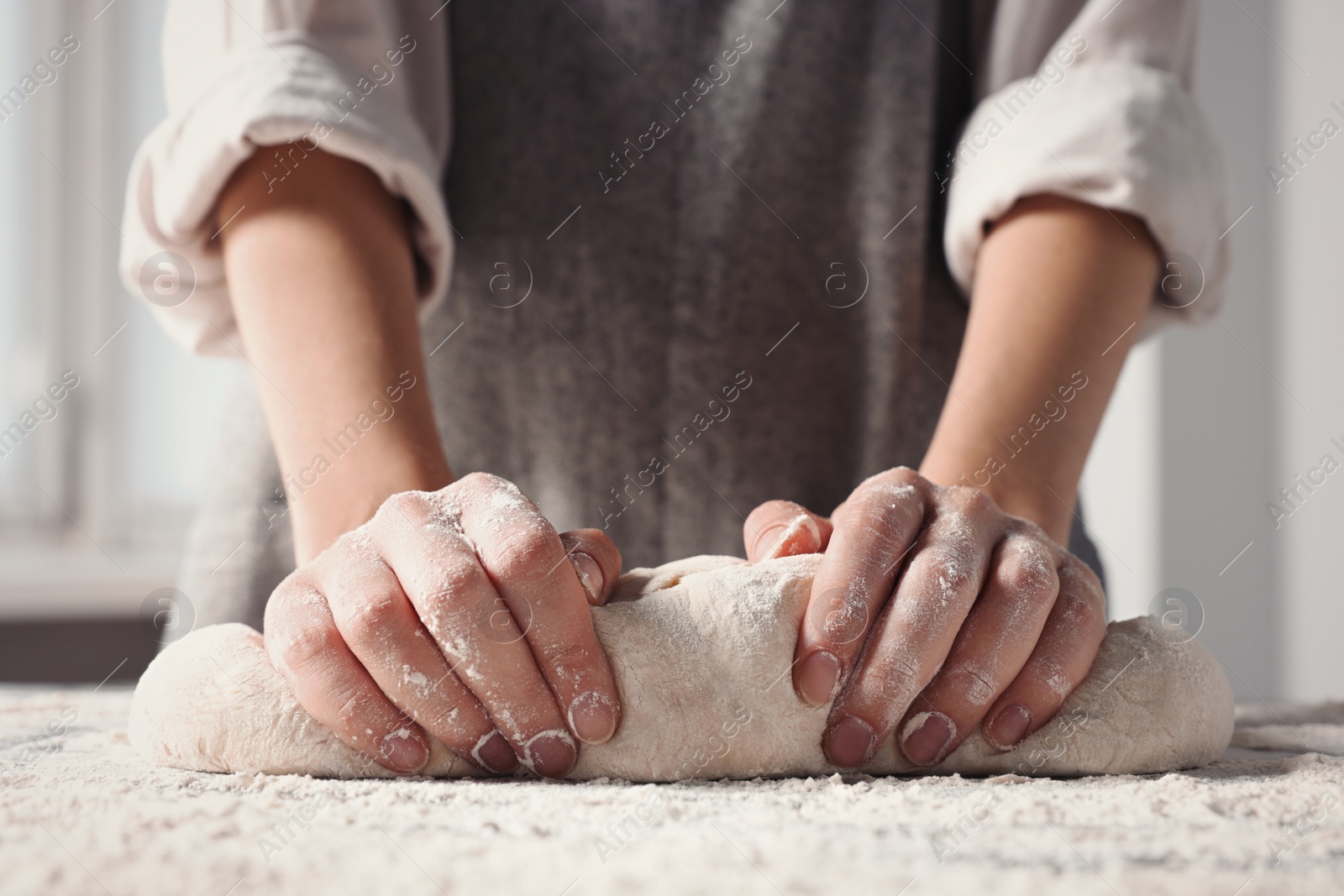 Photo of Woman kneading dough at table in kitchen, closeup