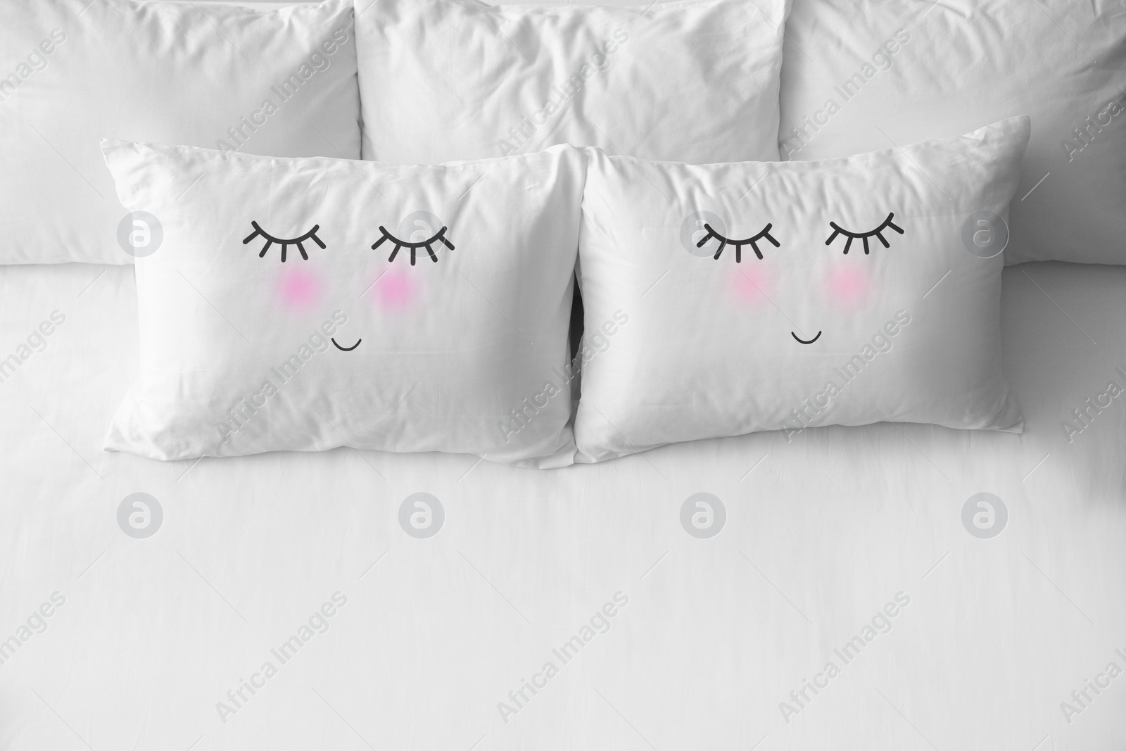 Image of Soft pillows with cute faces on comfortable bed, above view