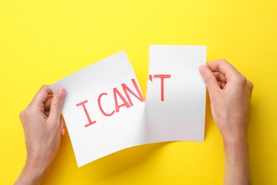 Motivation concept. Woman making phrase I Can from I Can't by tearing paper on yellow background, top view