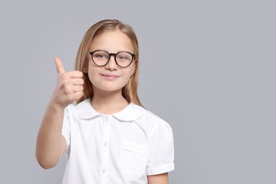Photo of Cute girl in glasses showing thumb up on light grey background. Space for text
