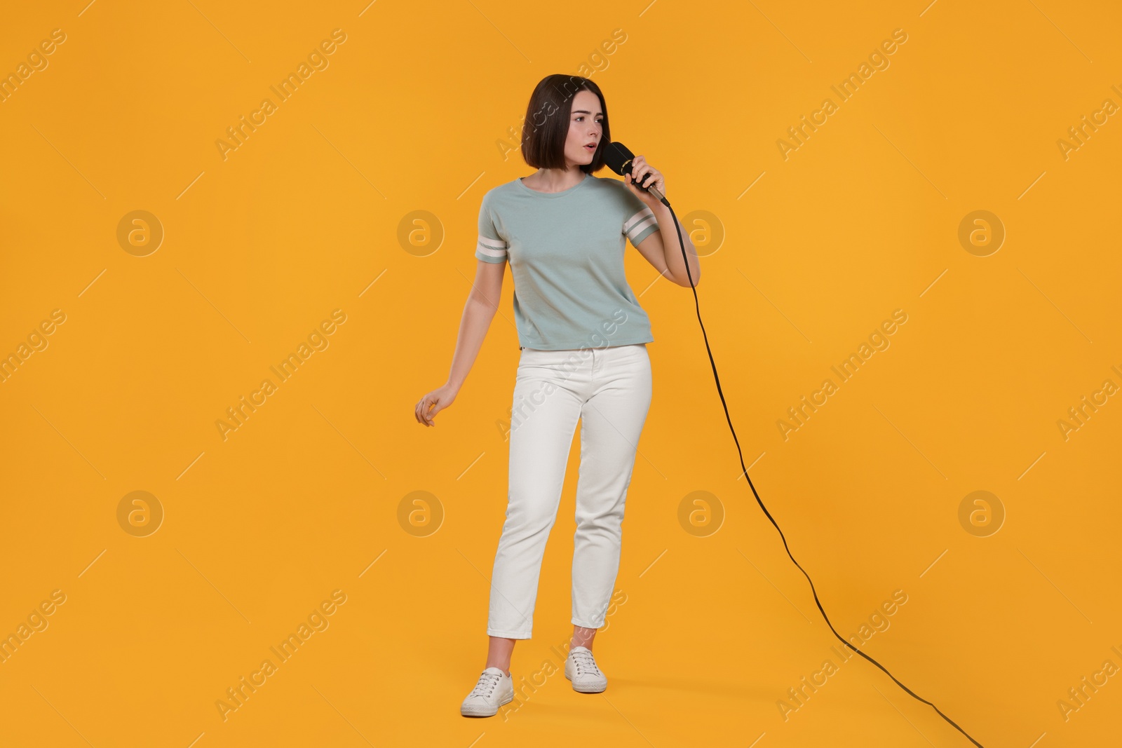 Photo of Beautiful young woman with microphone singing on yellow background