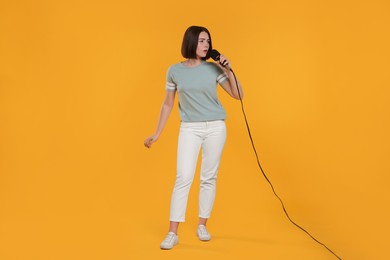 Beautiful young woman with microphone singing on yellow background