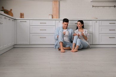 Photo of Happy couple sitting on warm floor in kitchen. Heating system