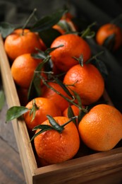 Photo of Wooden crate with fresh ripe tangerines and leaves on table, closeup