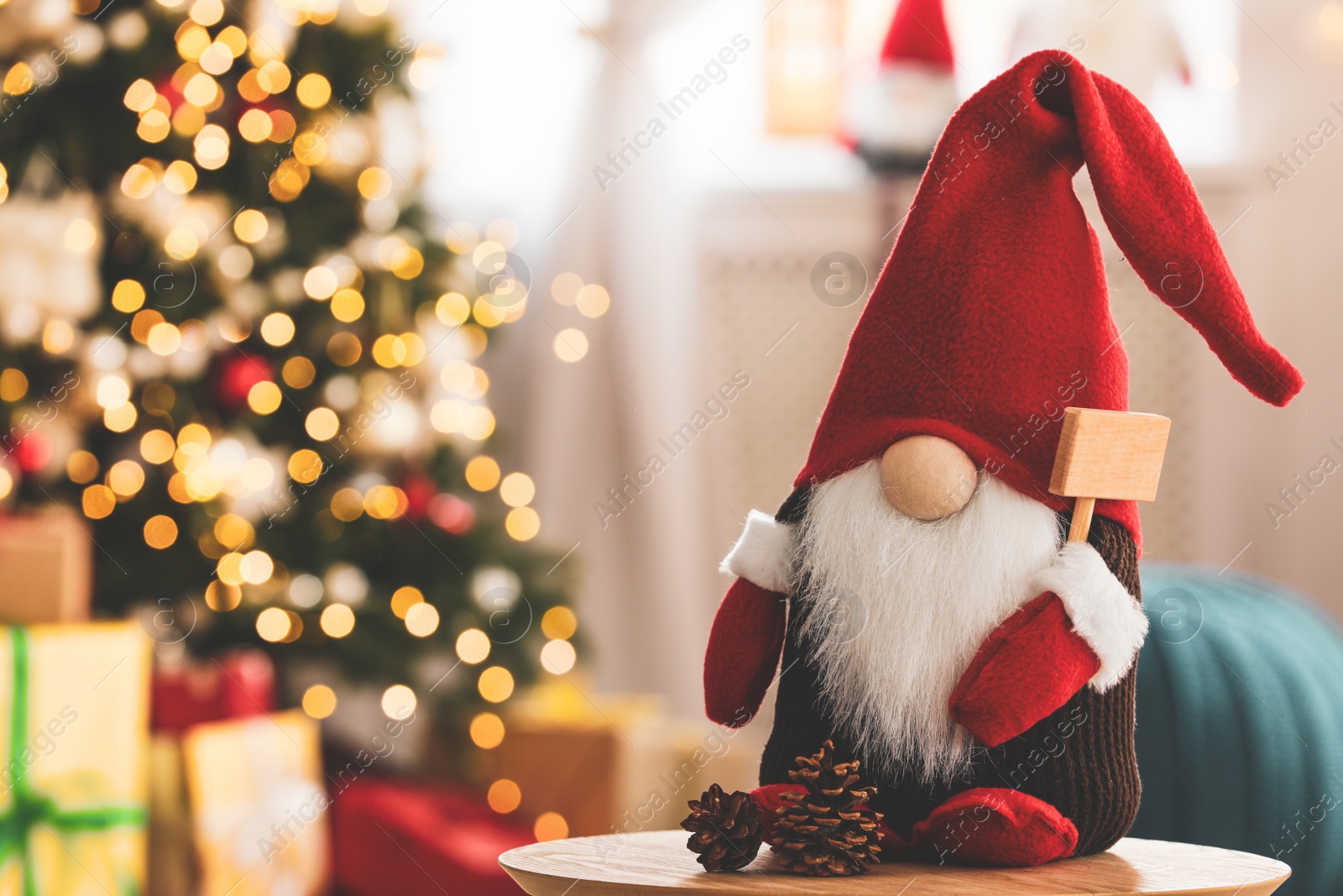 Photo of Cute Christmas gnome on wooden table in decorated room, space for text