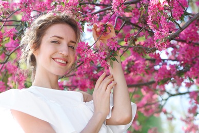 Attractive young woman posing near blossoming tree on sunny spring day