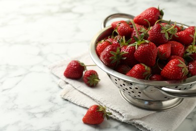 Photo of Metal colander with fresh strawberries on white marble table, space for text