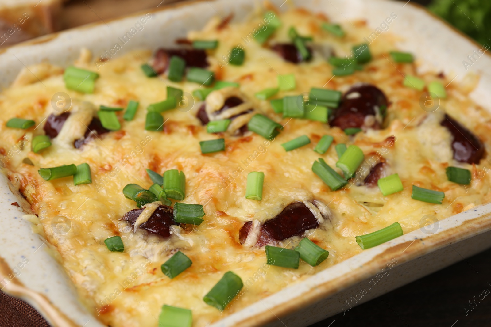 Photo of Tasty sausage casserole with green onions in baking dish on table, closeup