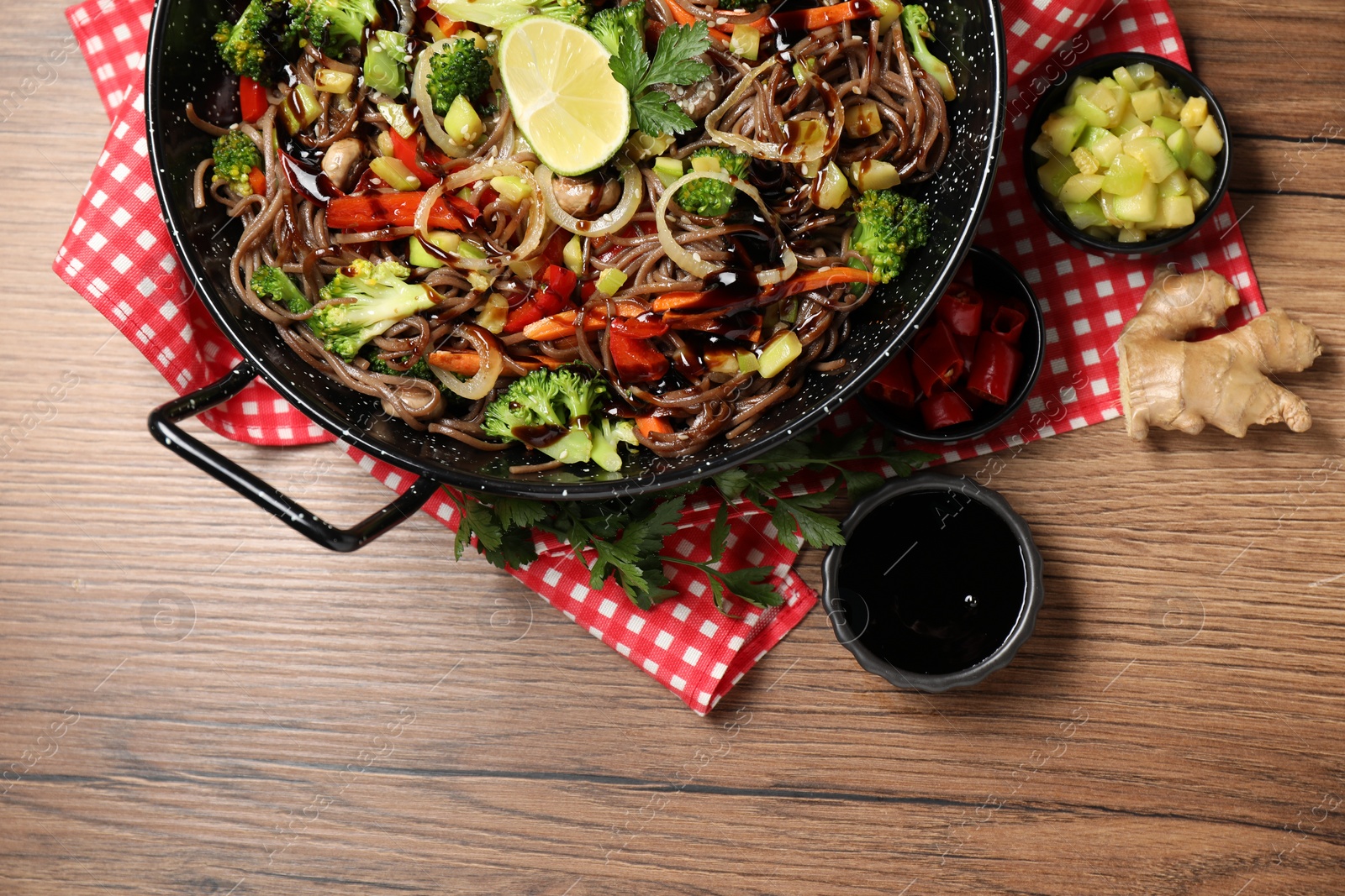 Photo of Stir-fry. Tasty noodles with meat in wok and ingredients on wooden table, flat lay