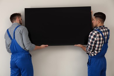 Photo of Professional technicians installing modern flat screen TV on wall indoors
